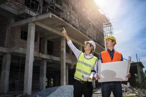 Businessman and engineer looking at a building blueprint at a high rise building construction site photo