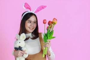 Mujer joven asiática vistiendo orejas de conejo sosteniendo un tulipán sobre un fondo de color rosa foto