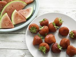 Fresas rojas maduras en un plato blanco y rodajas de sandía fresca en una vista superior de la placa verde foto