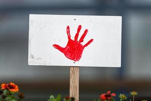 Shield with painted red hand stands in a flowerbed with copy space photo