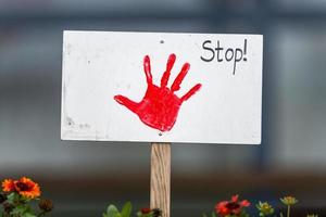 Sign with painted red hand stuck in a flowerbed in front of blurred background photo