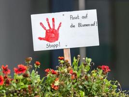 Sign with painted red hand stuck in a flowerbed with the german inscription Stop Watch the flowers photo