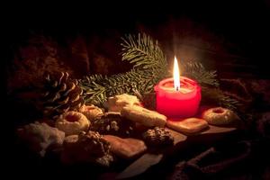 Burning red candle stands between decorated Christmas cookies on a wooden board