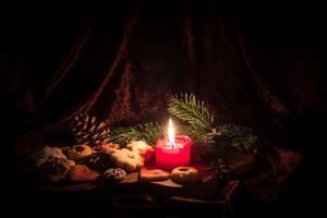 Burning red candle stands between decorated Christmas cookies on a wooden board photo