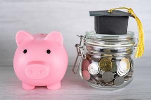 Save money coins in grass jar with piggy bank and graduation cap Business finance education concept photo