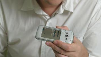 Un homme avec des lunettes examine un vieux téléphone avec un écran tactile cassé video