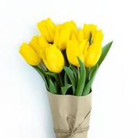 Ramo de tulipanes amarillos envueltos en papel artesanal sobre fondo blanco. foto