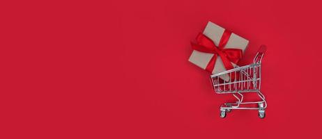 Carrito de supermercado y caja de regalo sobre fondo rojo con espacio de copia concepto de compras