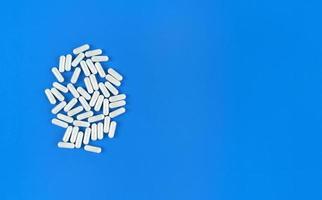 Cápsulas de píldoras dispersas blancas sobre fondo azul con espacio de copia