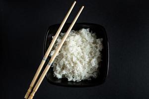 Bowl with boiled rice on black background photo