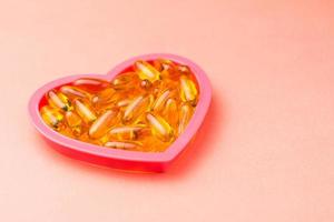 Fishoil capsules in the heart shape frame on pink background with copy space photo