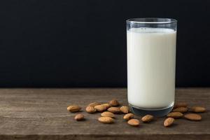 Leche de almendras y almendras en la mesa de madera con espacio de copia sobre fondo negro foto