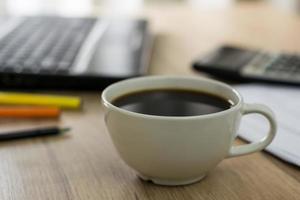 close up of a white coffee cup with laptop and Calculator on the office desk photo