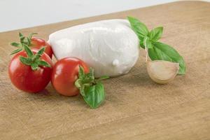 Mozzarella orgánica italiana con tomates cherry y albahaca sobre una tabla para cortar foto