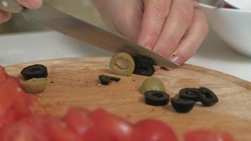 closeup de uma mulher na cozinha de casa cortando azeitonas em uma placa de madeira para pizza