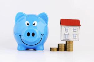 Saving money plan concept with blue piggy bank and paper house on coins stack on white background photo