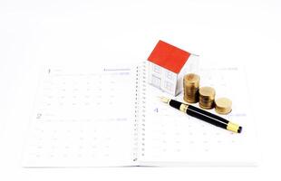 Mortgage loan planning concept with fountain pen and coins and paper house on calendar book pages photo