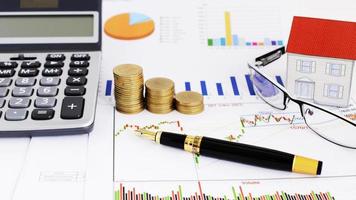 Stock investment concept with close up fountain pen and coins stack and calculator and paper house and eyeglasses photo