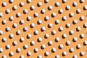 Minimal pattern made of white eggs under bright light with dark shadows on orange background photo