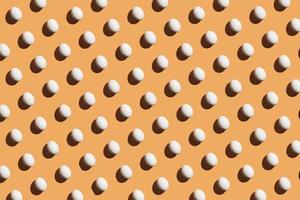 Minimal pattern made of white eggs under bright light with dark shadows on orange background photo