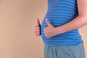 A close up view of the belly of a pregnant woman in a blue shows a like sign