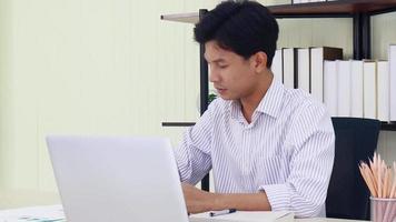 Hombre asiático está sentado en una oficina moderna con dolor debido a las largas horas de trabajo video