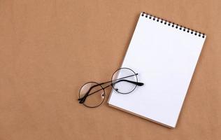 Flat lay top view photo of glasses and notepad on a beige background