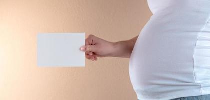 A close up view of the belly of a pregnant woman that is holding an empty sheet of paper photo