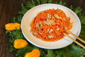 Ensalada de carne coreana de zanahoria con palillos en la mesa de madera de roble foto