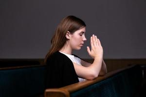 una niña cristiana con camisa blanca está sentada y orando con corazón humilde en la iglesia foto