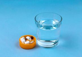 Glass of water and pills on blue background with copy space for text photo