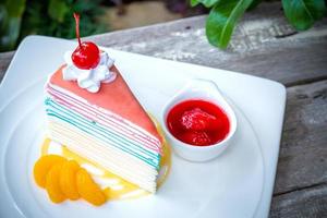 pastel de crepe arcoiris y una cereza con salsa de fresa foto