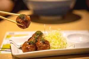 Primer plano de takoyaki, palillo sujetado en bola takoyaki sobre fondo de mesa de madera foto