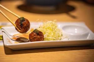 Closeup of takoyaki, chopstick clamped on takoyaki ball on wooden table background photo