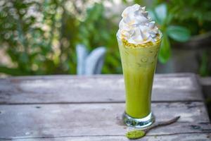 Ice matcha green tea with whipped cream on wooden table background photo