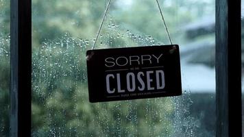 A closed sign hanging on the front door of the restaurant swaying on a rainy day video