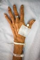 Mano del paciente anciano con enchufe en la cama en el hospital foto