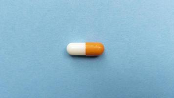 Orange and white single pill capsule on blue background Simple flat lay with pastel texture Medical concept Stock photo