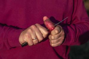 Close-up de un hombre caucásico en el bosque cortando finas rodajas de patata cruda con un cuchillo foto