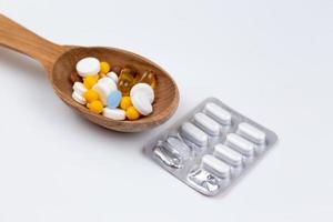 Medicine pills and drugs in a wood spoon on white background with copy space photo