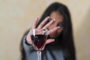 Renunciar al alcohol una mujer joven en la mesa rechaza una copa de vino tinto con la mano foto