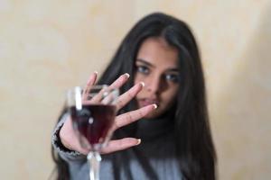 Renunciar al alcohol una mujer joven en la mesa rechaza con la mano una copa de vino tinto foto