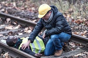 African American railroad engineer injured in an accident at work on the railway tracks while his coworker helps him photo