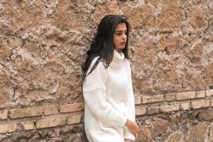 Young contemplative brunette woman leaning against a brick wall photo