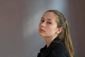 Tiro de tres cuartos o retrato de semi perfil de una bonita adolescente con el pelo de cola de caballo posando mirando a la cámara sobre un fondo gris foto