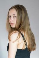 Studio portrait of a young back turned woman turning her head looking at the camera over a grey background photo