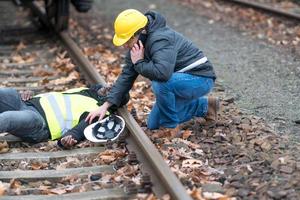 African American railroad engineer injured in an accident at work on the railway tracks His coworker using his cell phone to call 911 photo