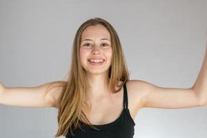 Retrato de estudio de una mujer joven sonriente posando sobre un fondo gris mostrando sus axilas depiladas foto