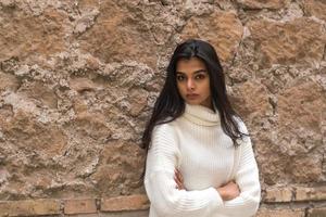 Portrait of a young romantic brunette woman leaning against a brick wall with crossed arms photo