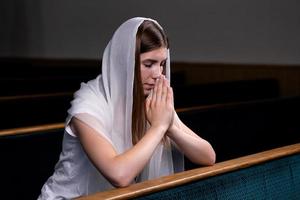 A young modest girl with a handkerchief on her head is sitting in church and praying